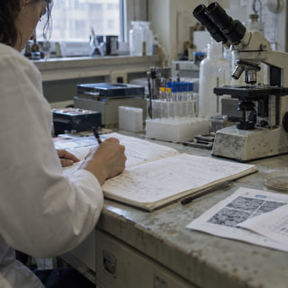 Ricercatrice prende appunti accanto a un microscopio in un laboratorio.