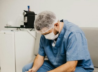 Infermiere seduto in ospedale con postura stanca e testa chinata